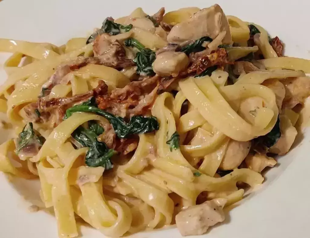A plate of creamy chicken pasta with spinach and sun-dried tomatoes